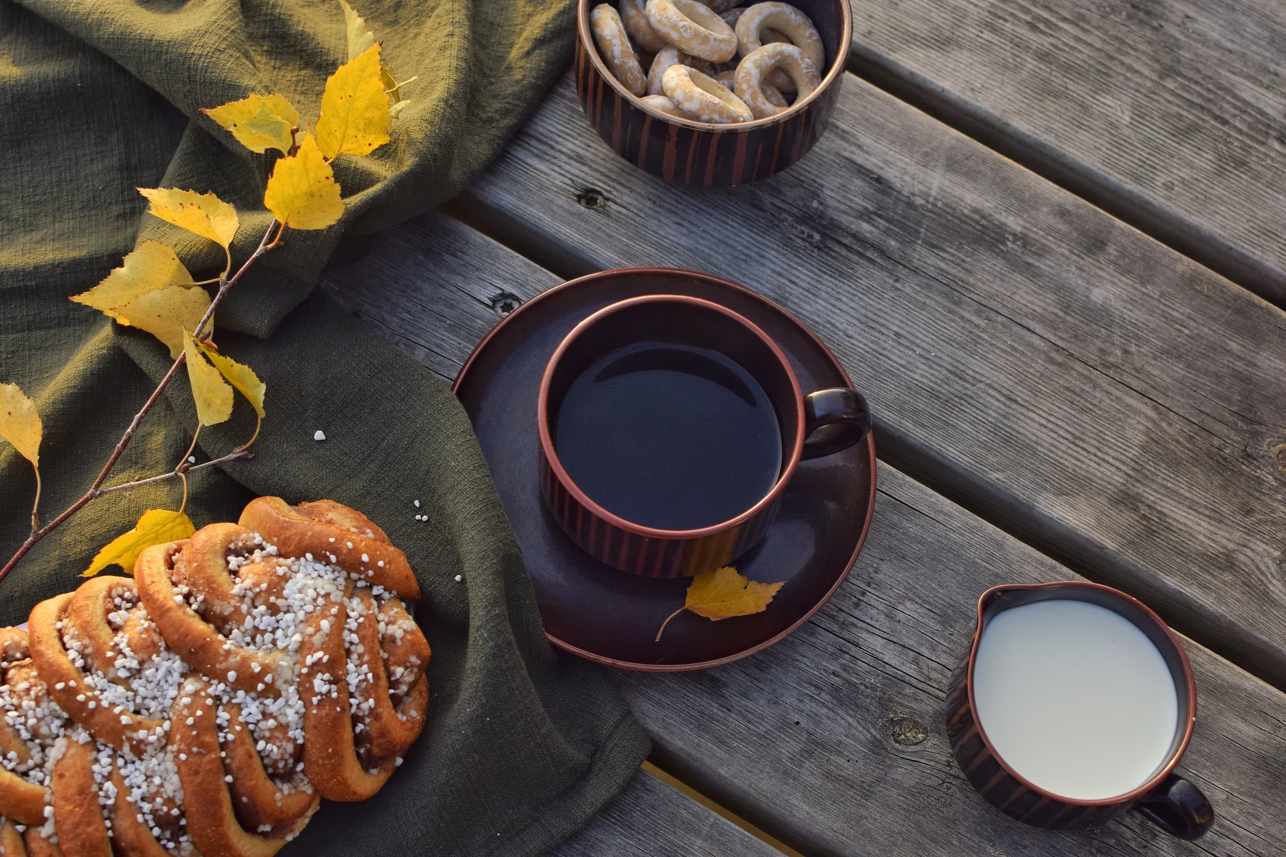 Tasse Kaffee mit Milch und Zimtschnecke auf Holztisch, dekoriert mit Herbstlaub.
