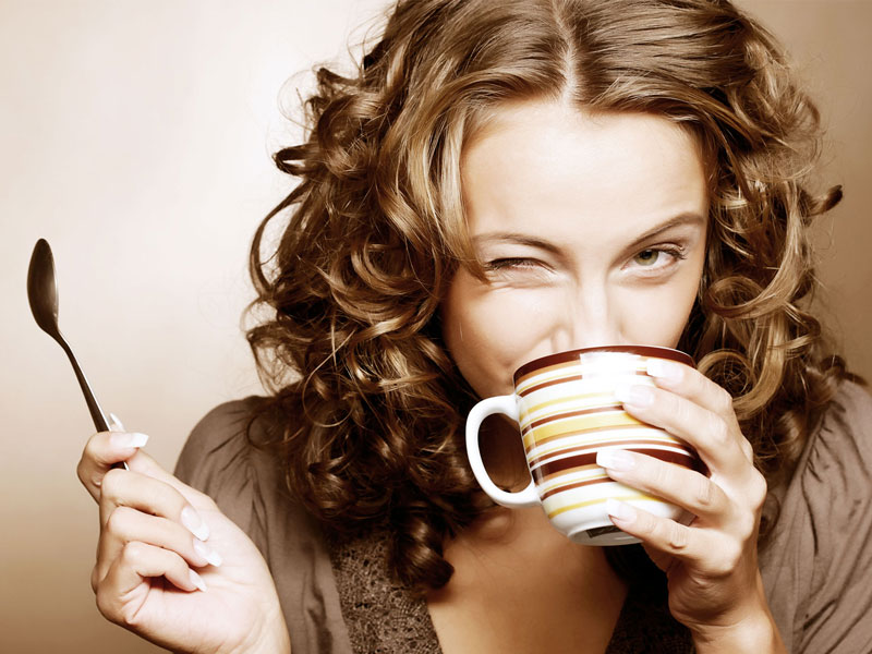 Frau mit lockigem Haar trinkt laechelnd eine Tasse Kaffee.