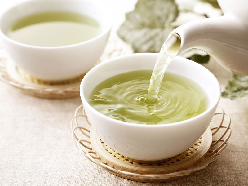 Frisch aufgegossener gruener Tee wird aus einer Kanne in eine weiße Schale gegossen.