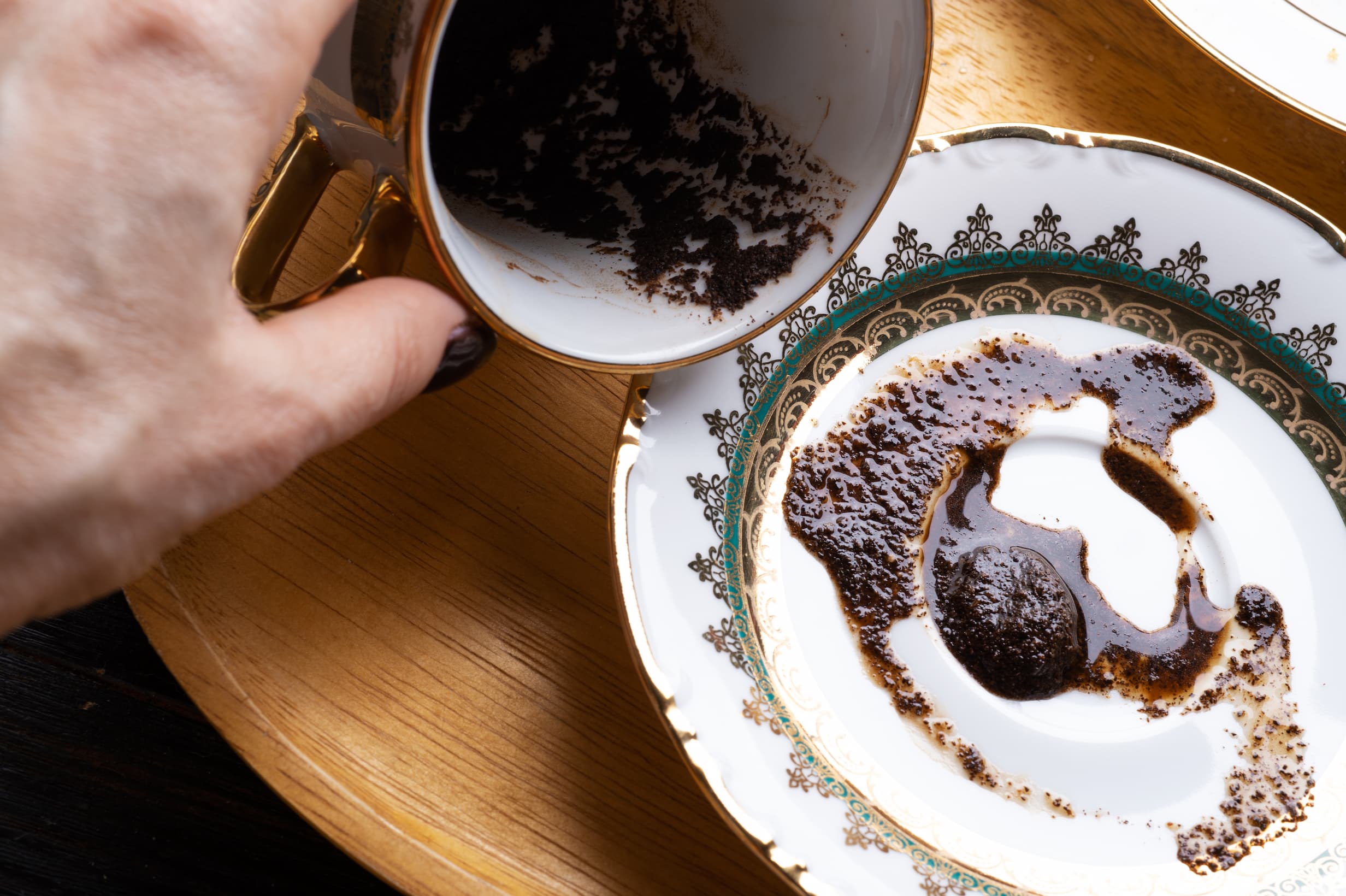 Hand haelt eine Tasse mit Kaffeesatz, der auf einen Unterteller gegossen wurde – traditionelle Kaffeesatzlesung.