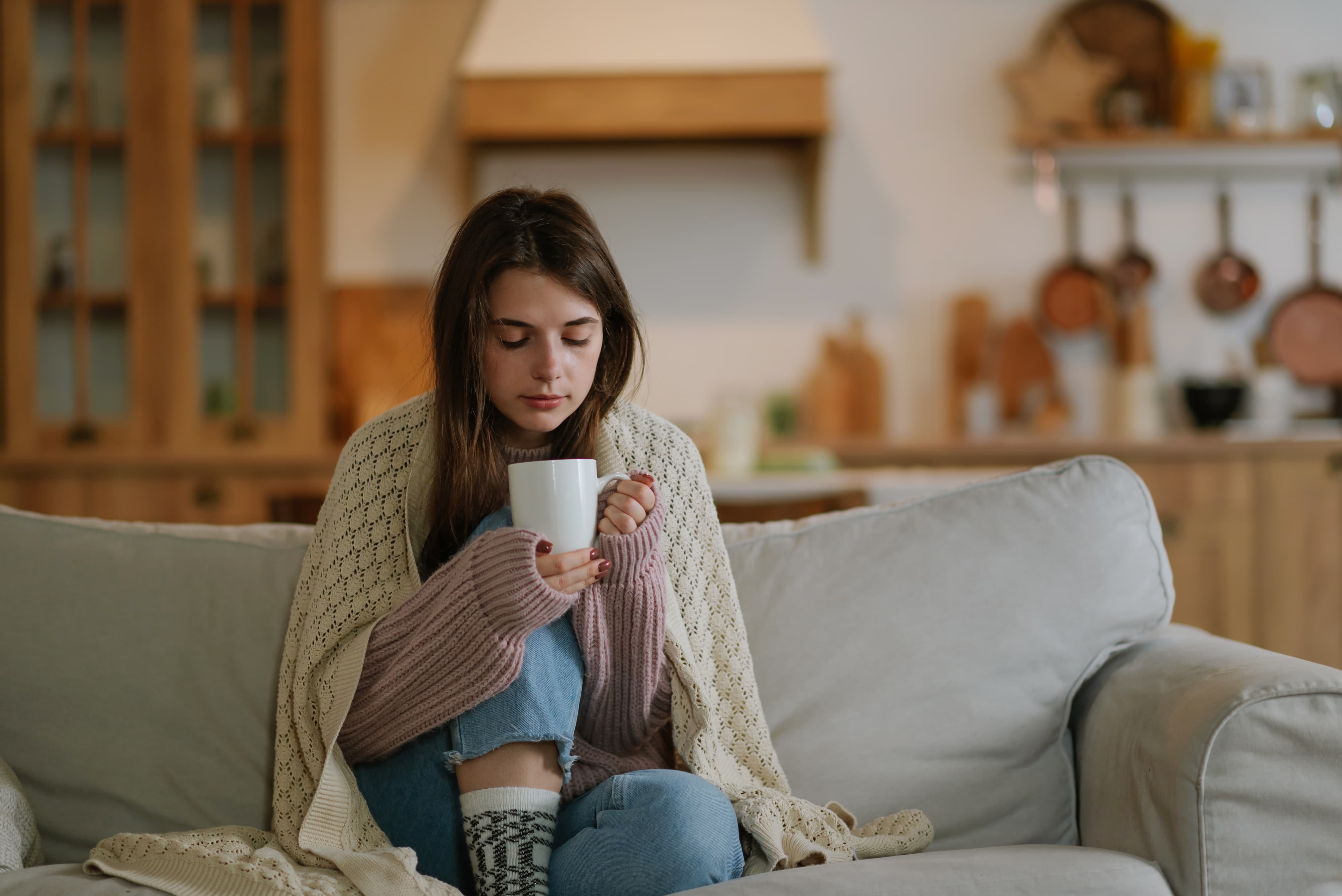Frau mit Strickjacke und Tasse Kaffee entspannt auf dem Sofa.