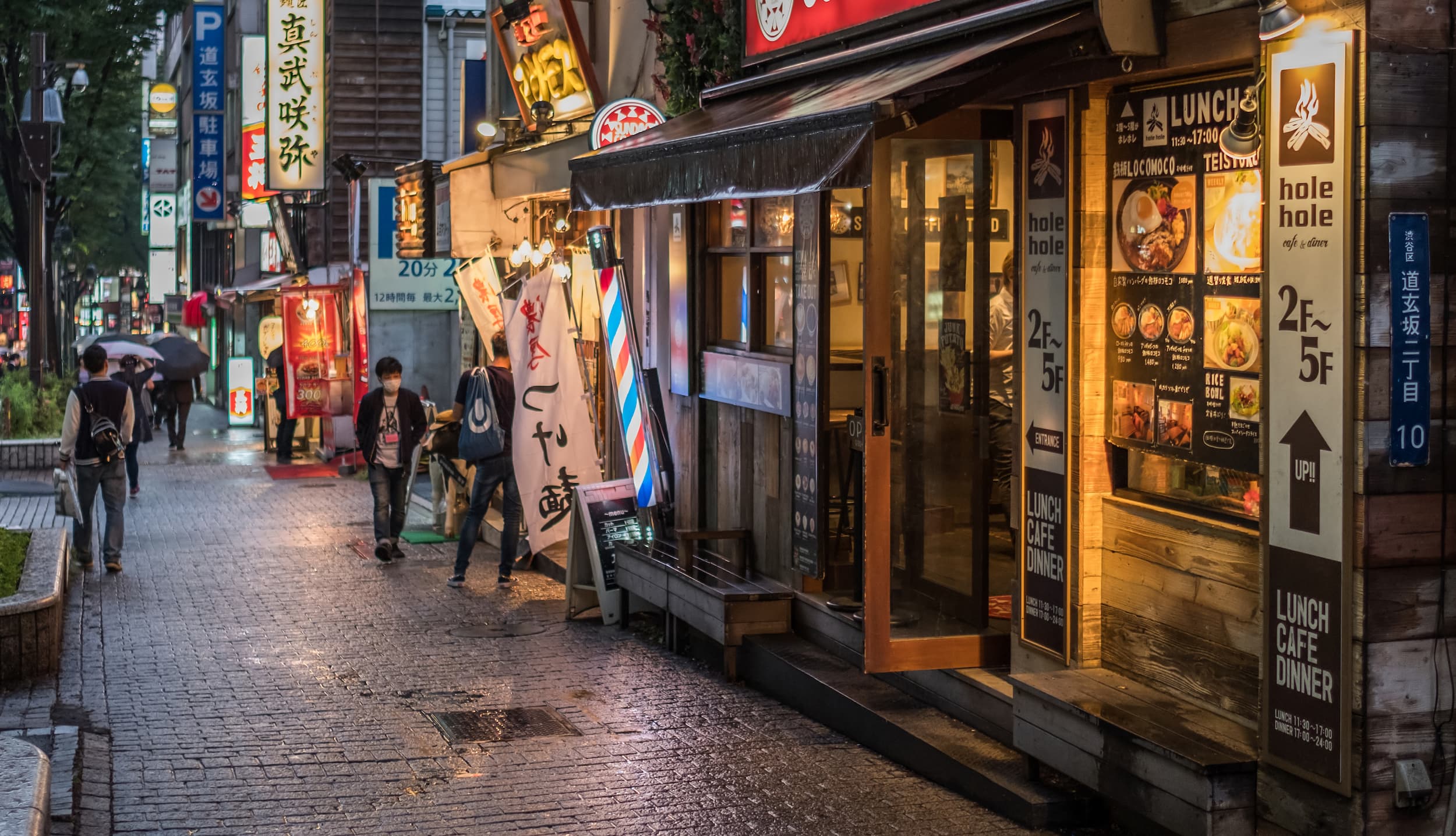 Abendliche Straßenszene in Japan mit Restaurants, Cafés und leuchtenden Schildern.