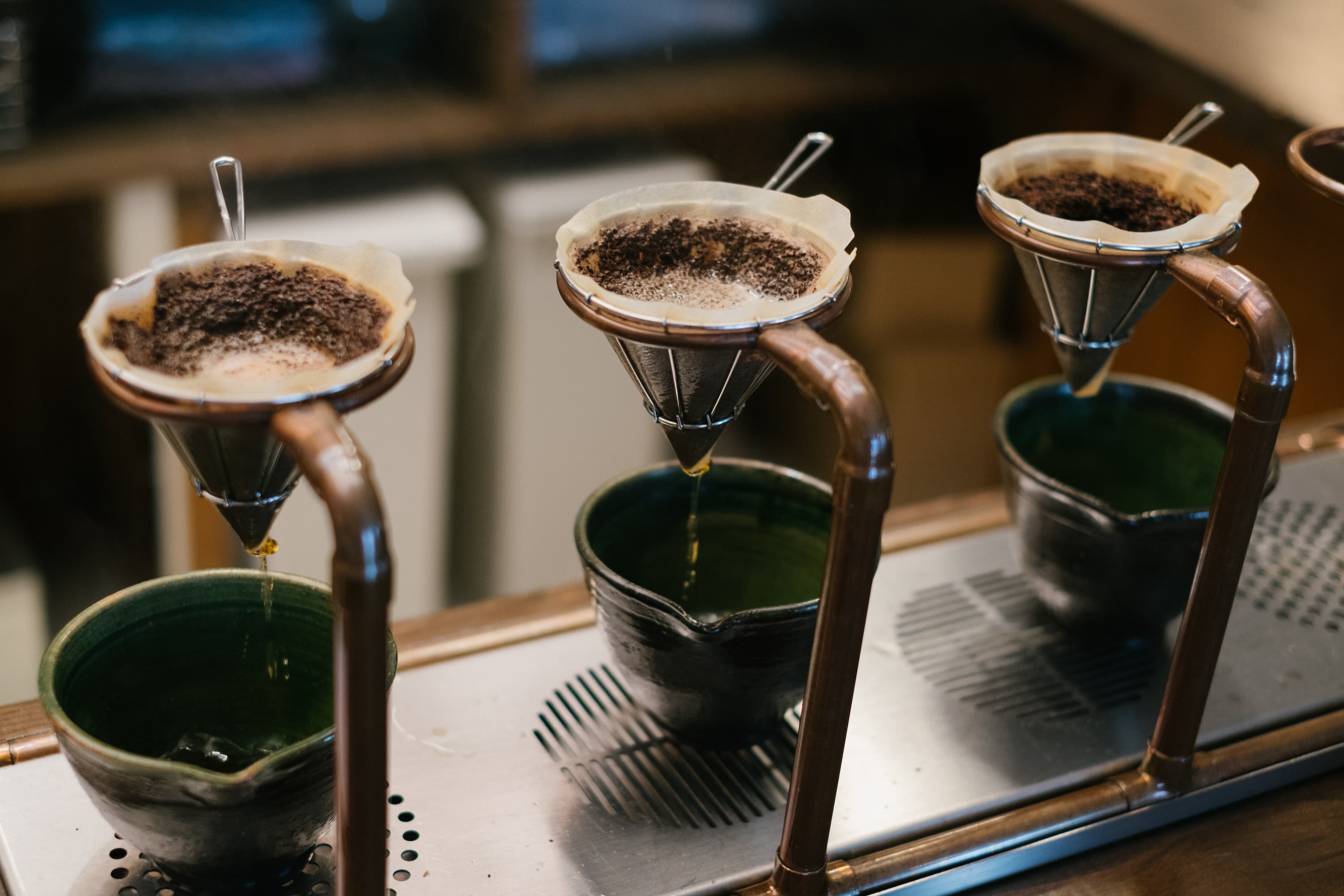 Mehrere Handaufguss-Kaffeefilter mit frischem Kaffeepulver, durch die Wasser tropft.