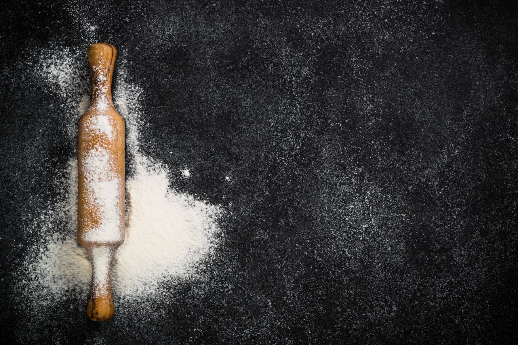 Nudelholz mit verstreutem Mehl auf schwarzem Tisch, Backen in der Küche.