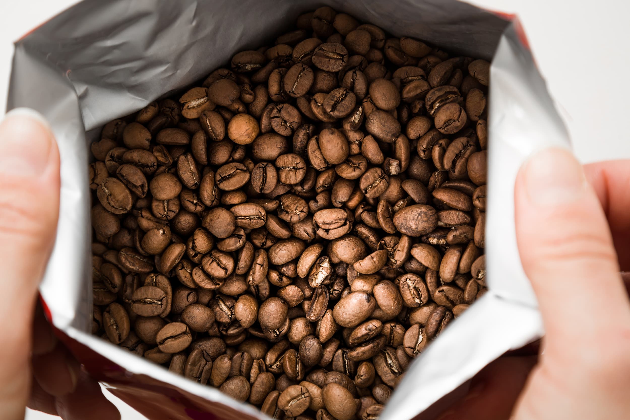 Hände öffnen Kaffeeverpackung mit frisch gerösteten Bohnen.
