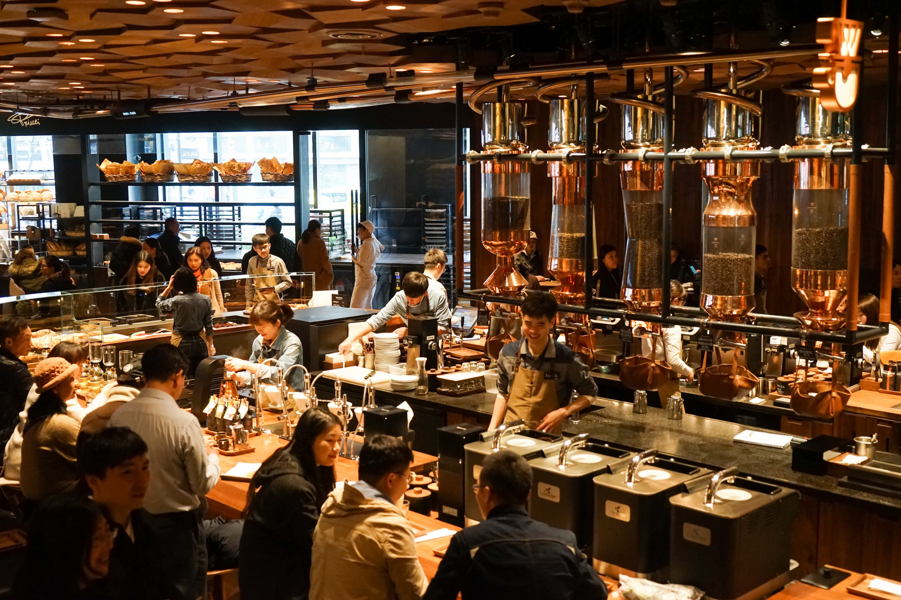 Gäste und Baristas in der Starbucks Reserve Rösterei mit großen Kaffeebehältern.