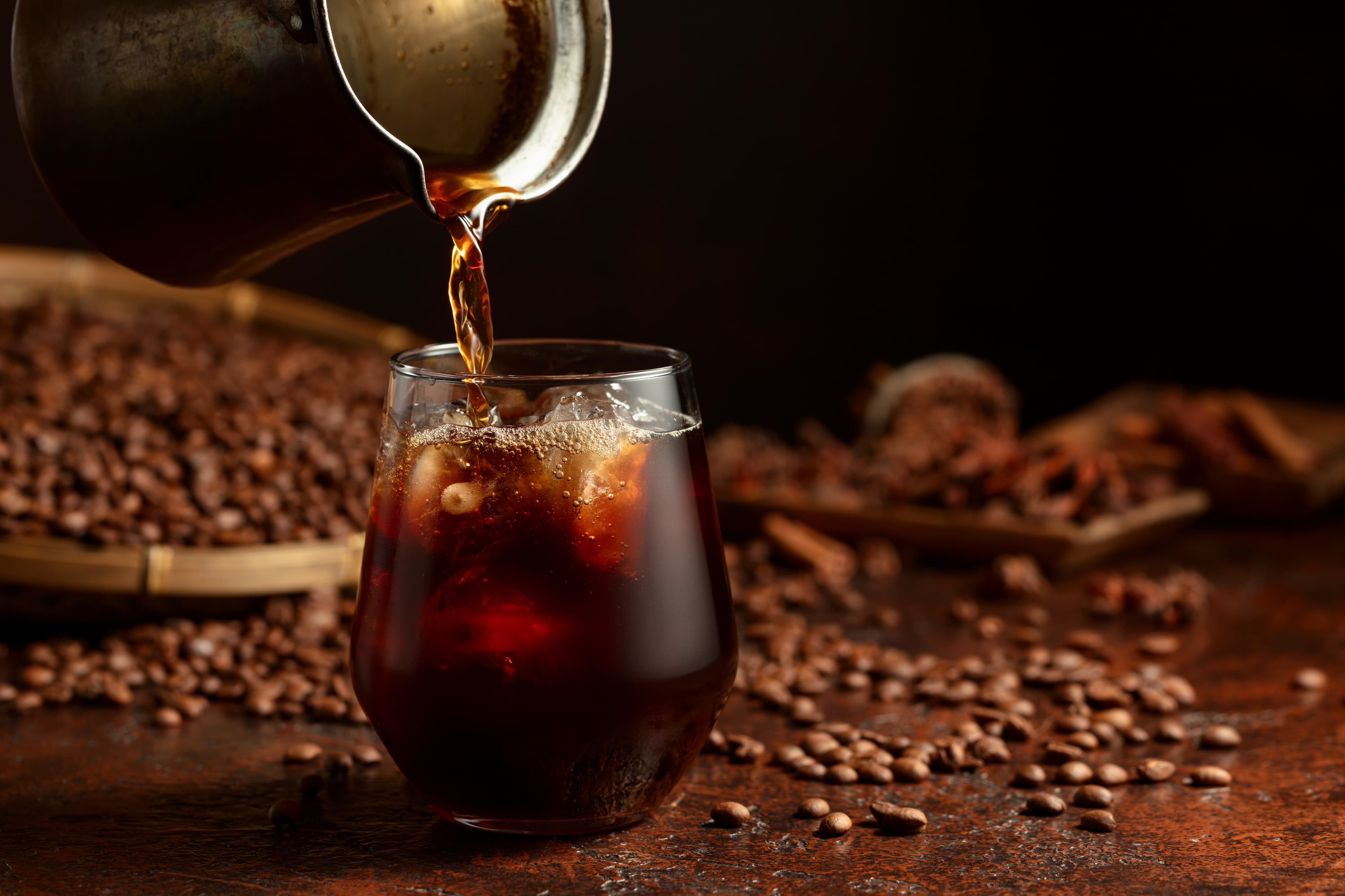 Eisgekühlter Cold Brew Kaffee wird in ein Glas mit Eiswürfeln gegossen.