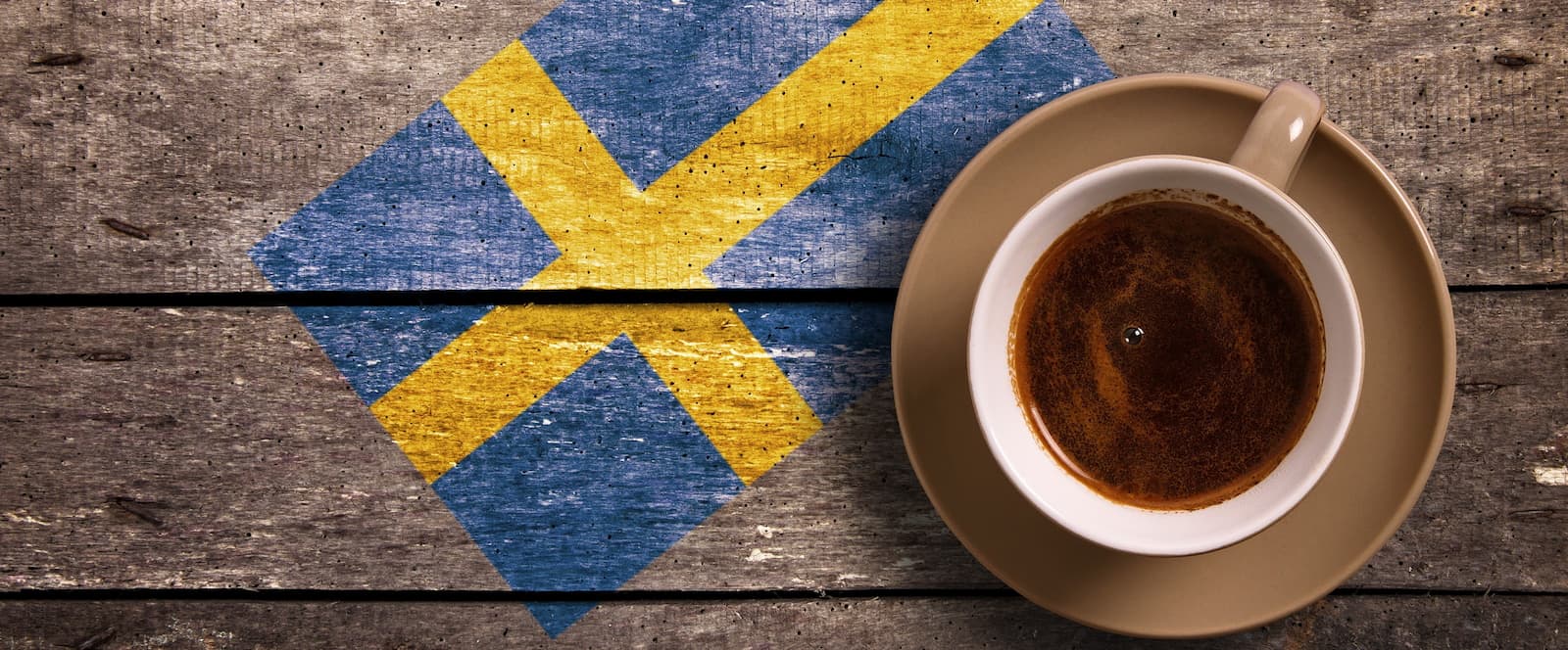 Tasse Kaffee auf Holzuntergrund mit schwedischer Flagge, Symbol für Fika Kaffeekultur.