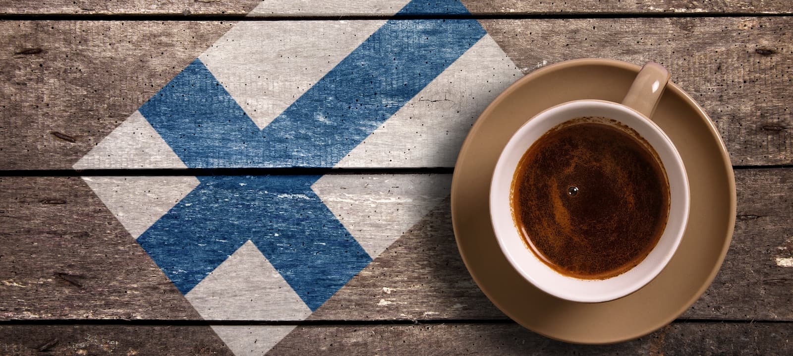 Tasse Kaffee auf Holz mit aufgemalter finnischer Flagge – Symbol für Kaffeekultur in Finnland.