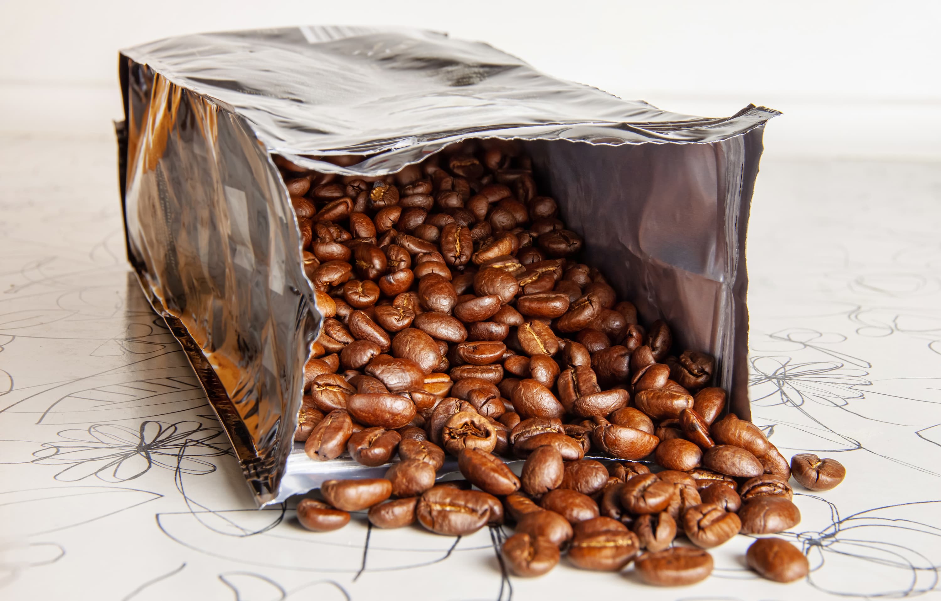 Silberne Kaffeeverpackung, aus der frische Kaffeebohnen herausfallen.