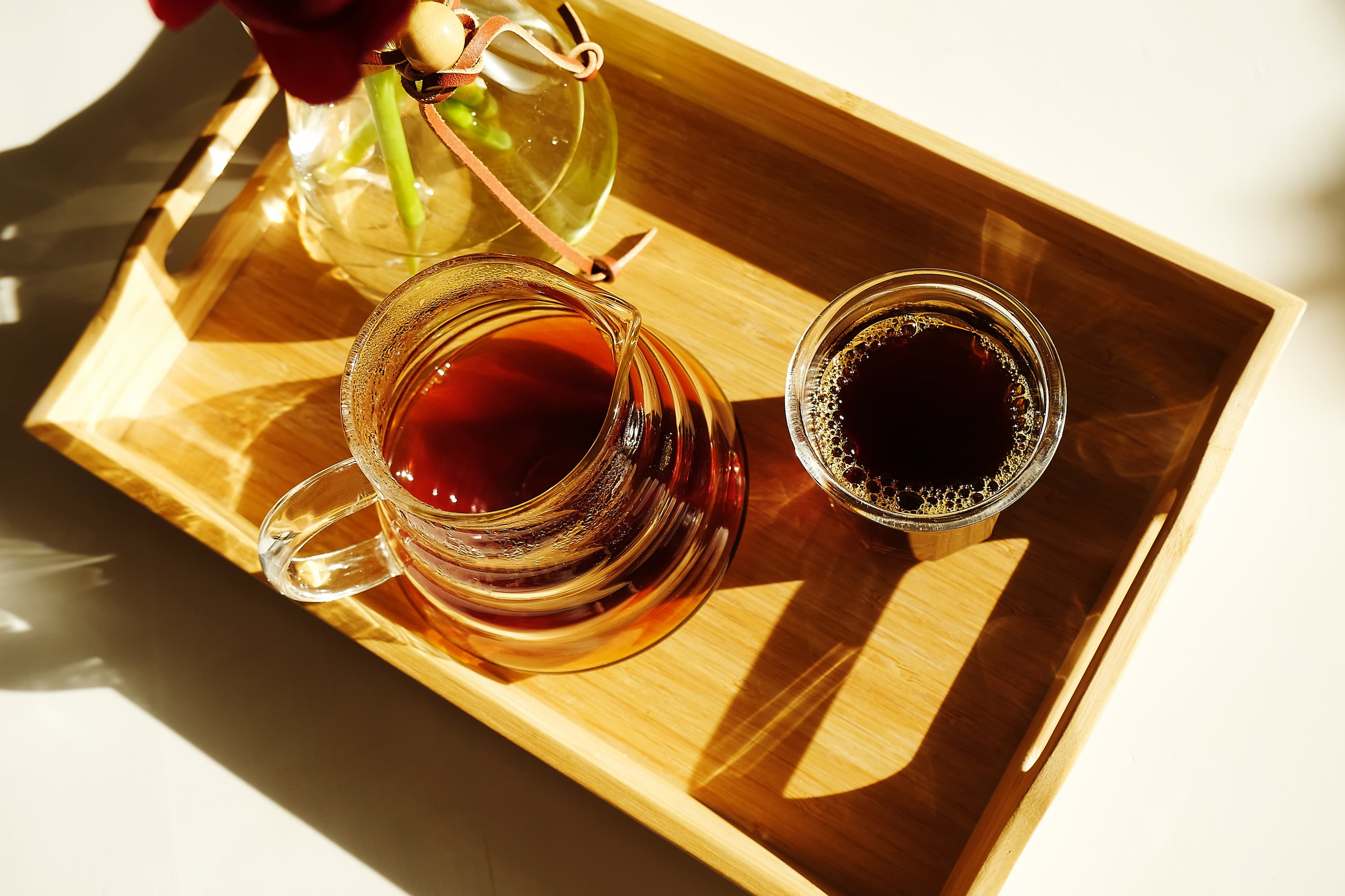 Glaskanne und Glas mit Kaffee auf Holztablett im Sonnenlicht serviert.