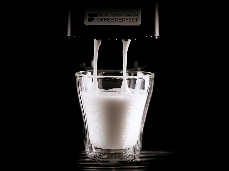 Eine Tasse Milch unter einer laufenden Kaffeemaschine Eine Tasse Milch unter einer laufenden Kaffeemaschine