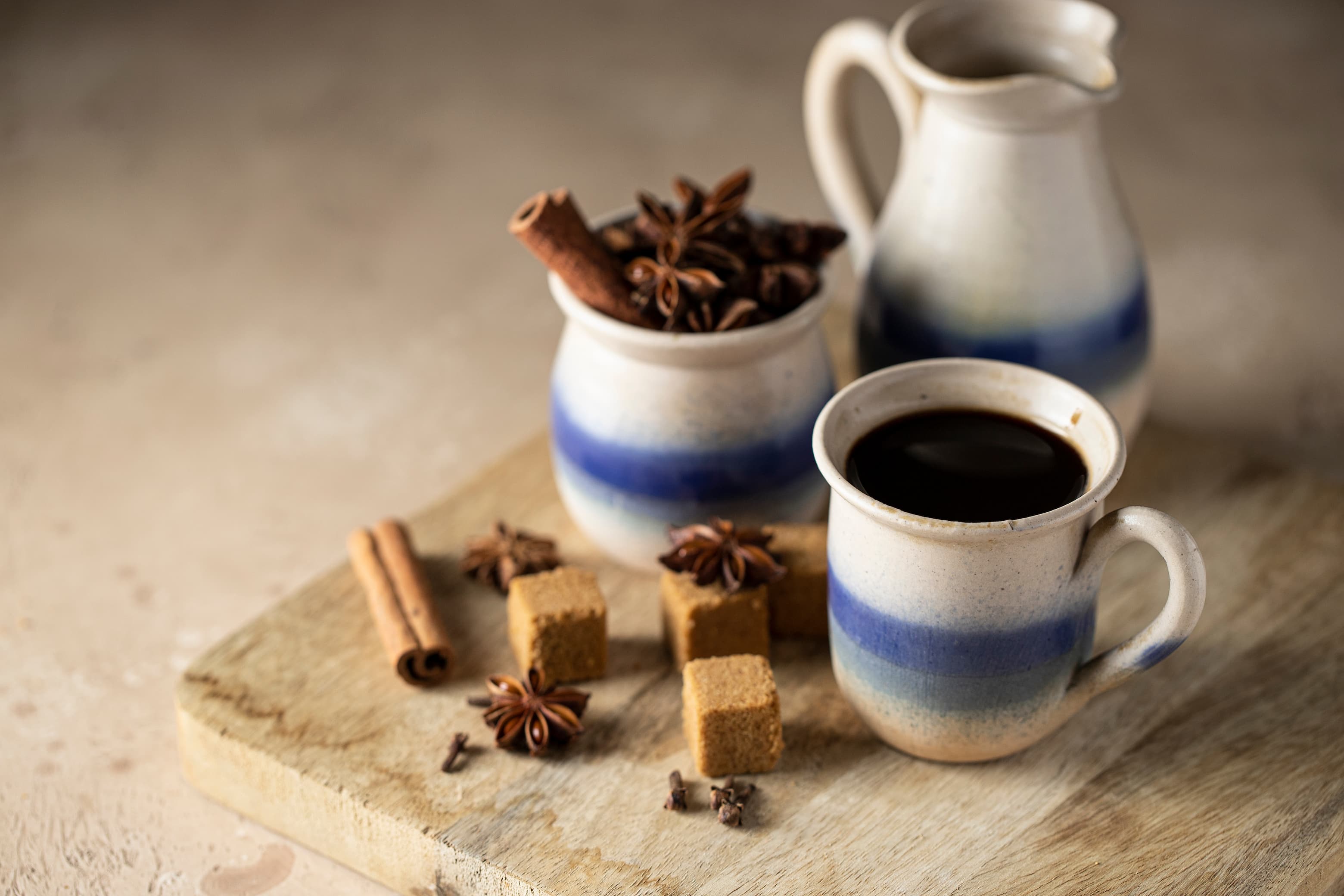 Tasse schwarzer Kaffee mit braunem Zucker, Zimt und Anis auf rustikalem Holzbrett.