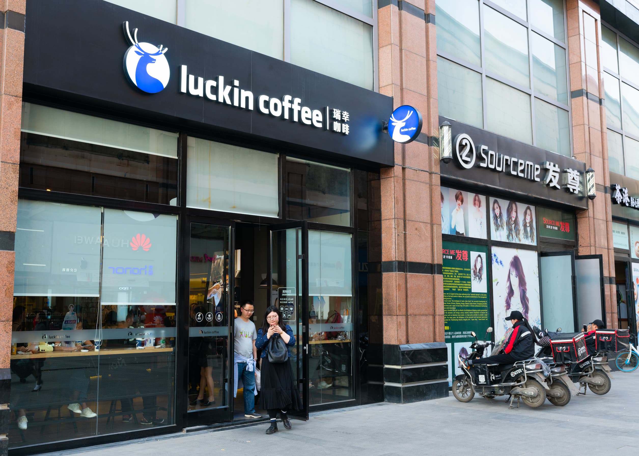 Außenansicht eines Luckin Coffee Cafés in China mit Passanten und Motorraedern davor.