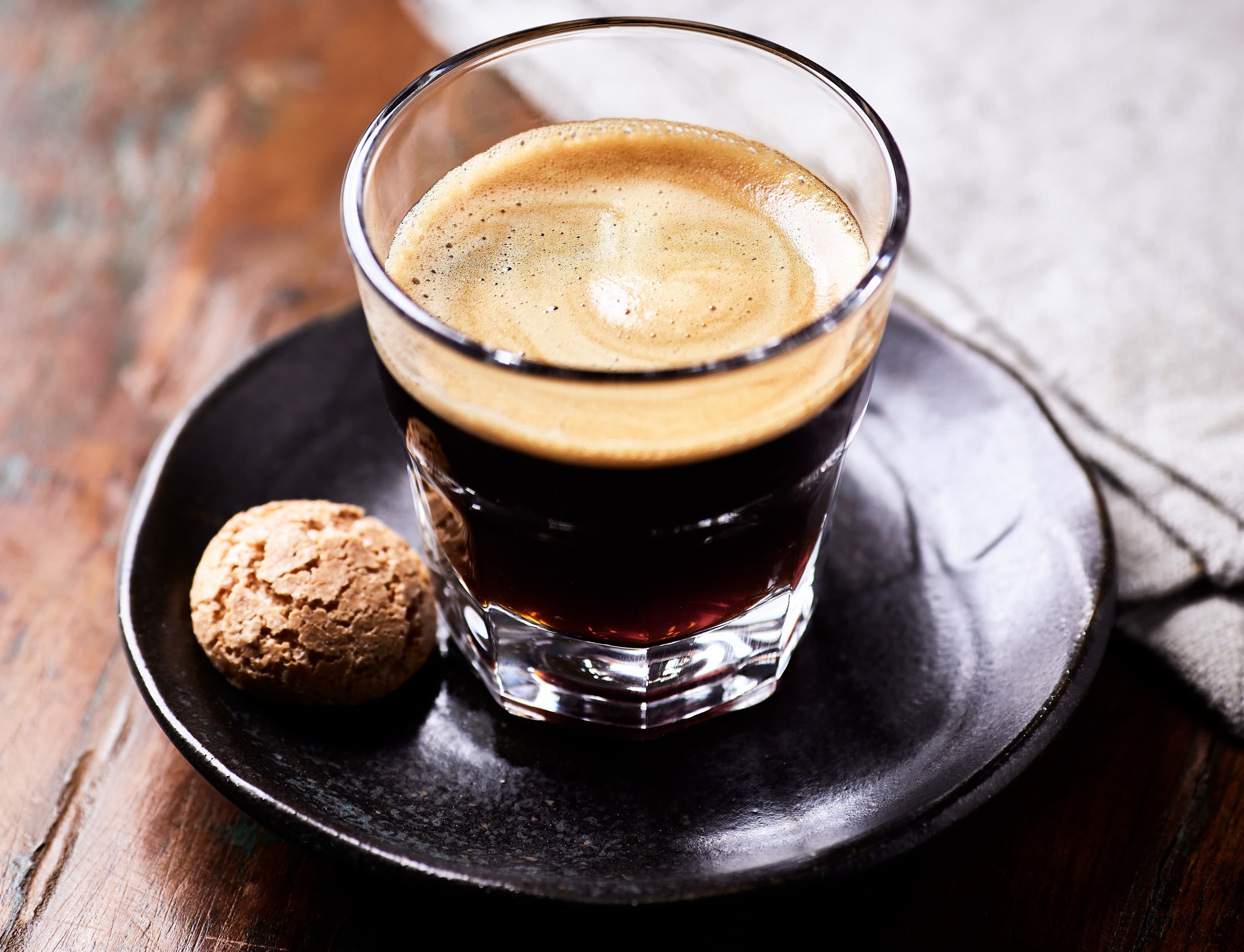Frisch gebrühter Espresso im Glas, serviert auf Teller mit Keks.