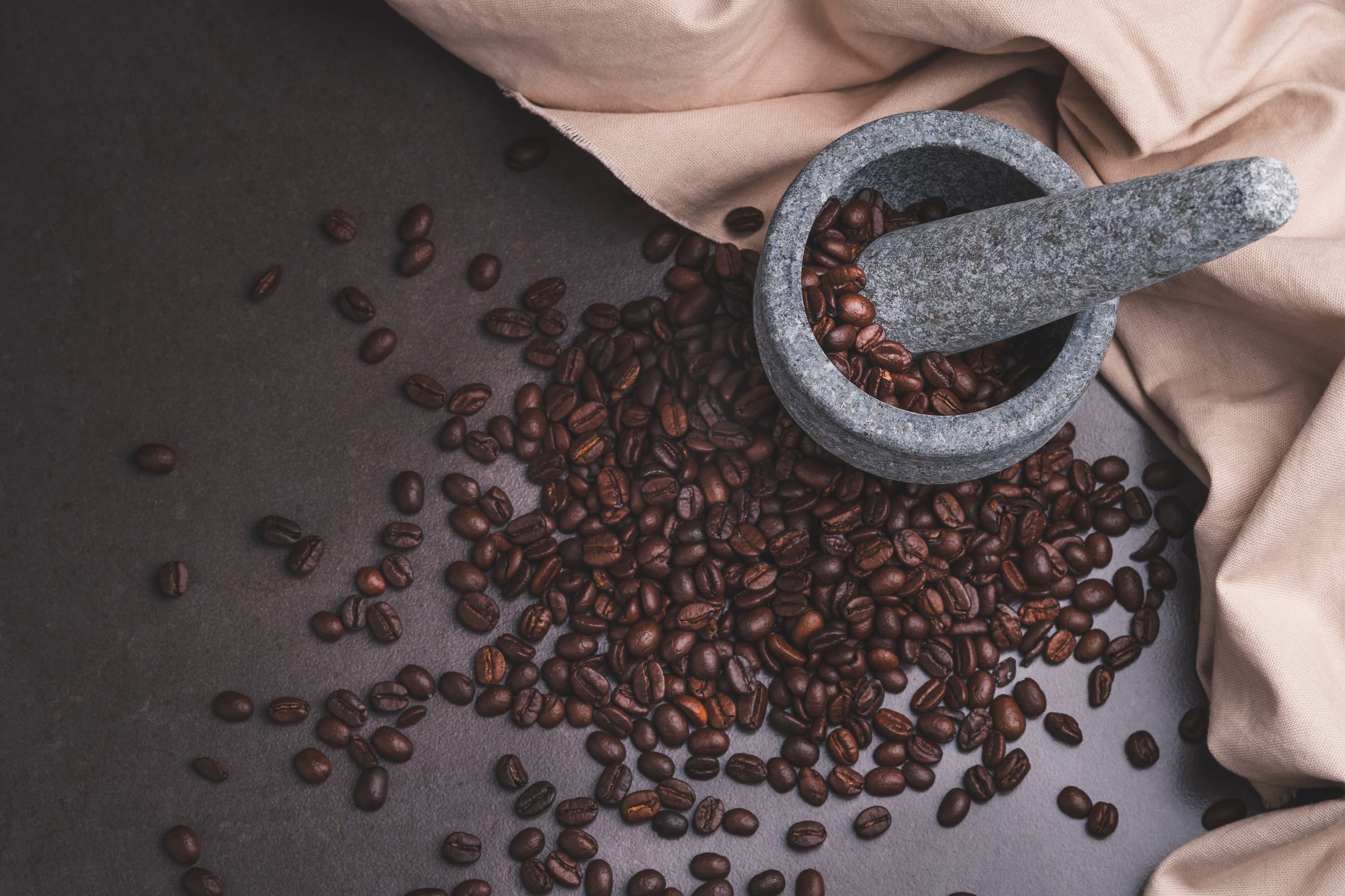 Frische Kaffeebohnen auf dunklem Untergrund mit Moerser und Stoeßel aus Stein.