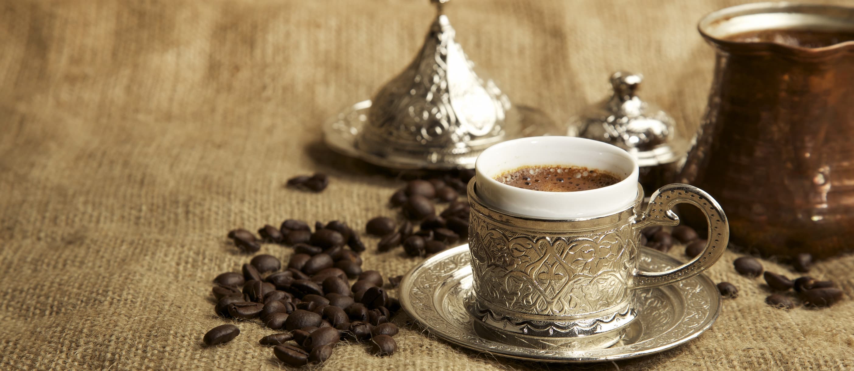 Eine Tasse orientalischer Kaffee im traditionellen Silberbecher mit Untertasse und Kaffeebohnen.