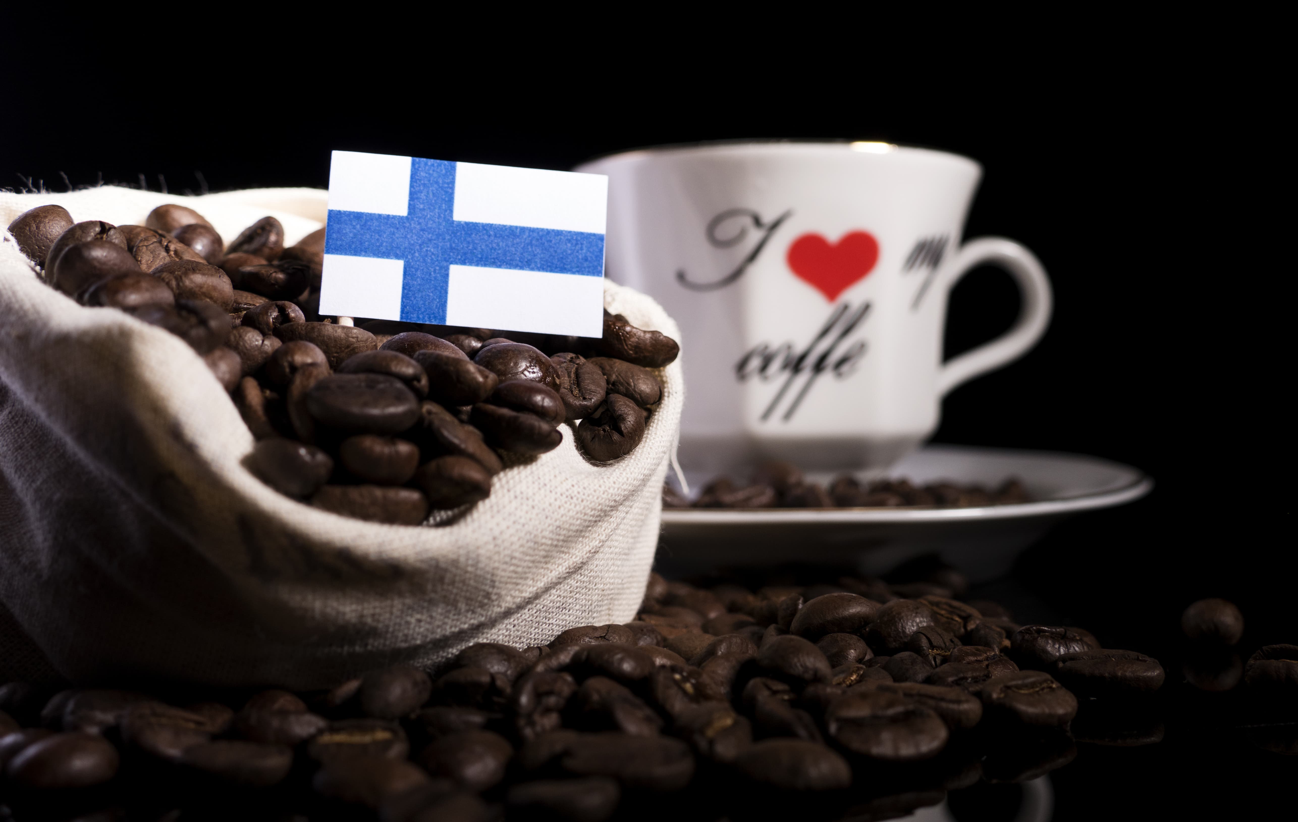 Sack mit Kaffeebohnen, darin kleine finnische Flagge, im Hintergrund eine Kaffeetasse.