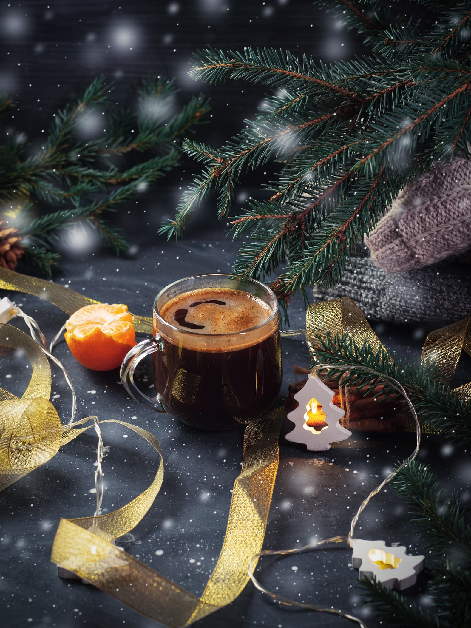 Tasse Kaffee mit Tannenzweigen, Weihnachtslichtern und goldener Deko.