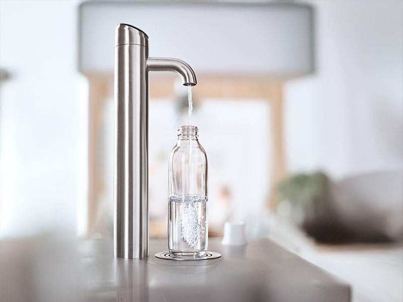 BRITA BR55 Wassserspender mit Edelstahl-Wasserhahn befüllt transparente Flasche in heller Umgebung.