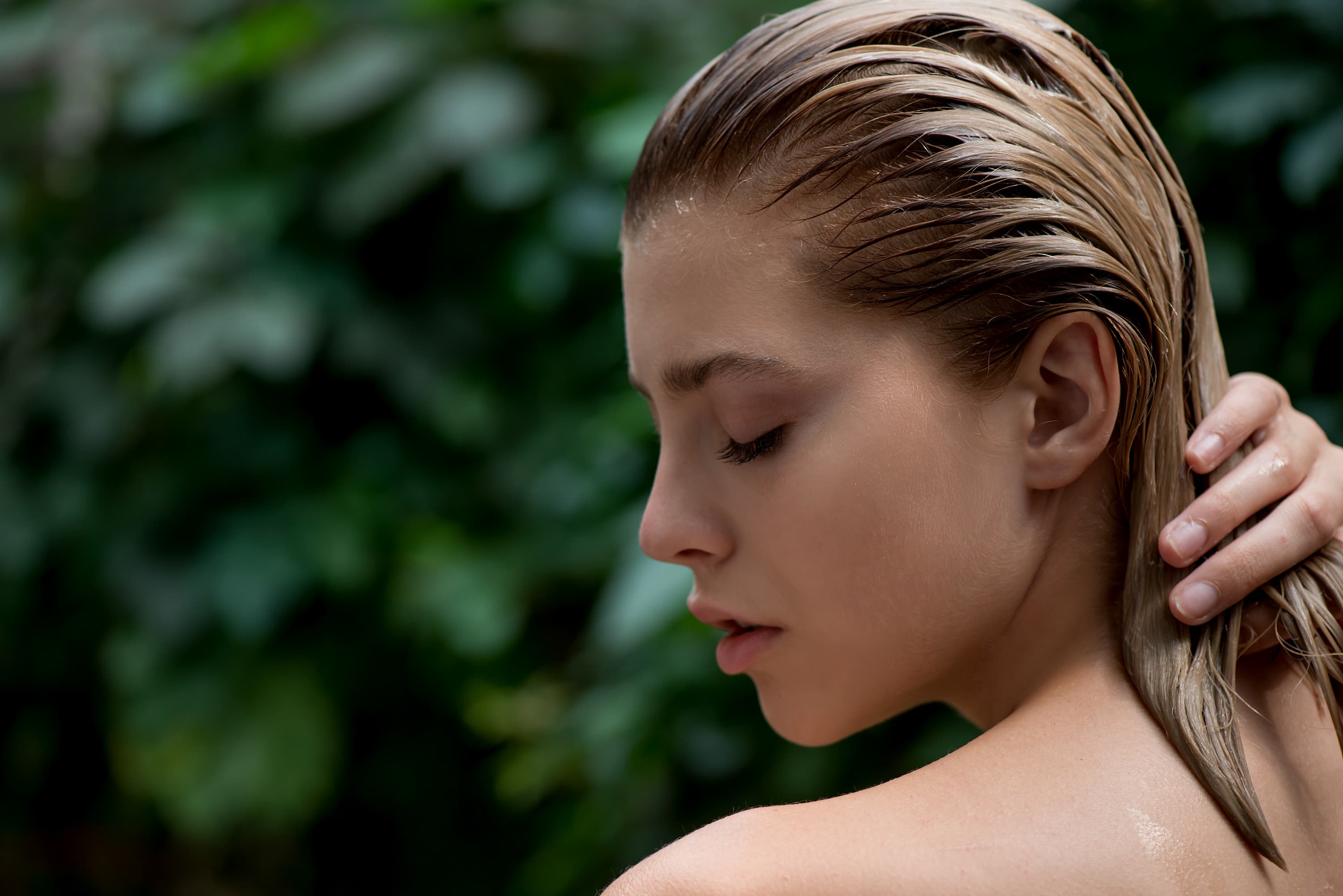 Portraet einer Frau mit nassen Haaren vor unscharfem gruenem Hintergrund.
