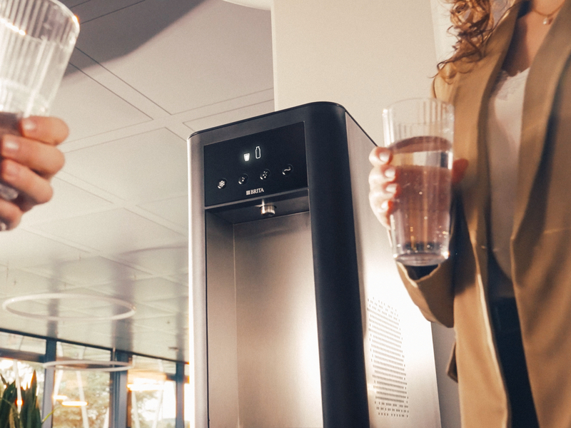Zwei Personen genießen frisches Wasser an einem BRITA BR50 Wasserspender im Büro.